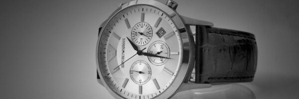 Elegant black and white close-up of a luxury wristwatch with a reflective stainless steel body and leather strap.